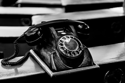Black and white photo of a classic rotary phone with dial, receiver and cord.