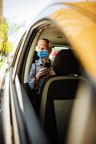 essential worker with face mask during lockdown in taxi, going to work - old men car vertical imagens e fotografias de stock