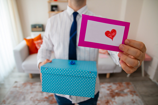 young crooked man holding a blue gift box in his hand and holding a gift card with a heart in the other hand