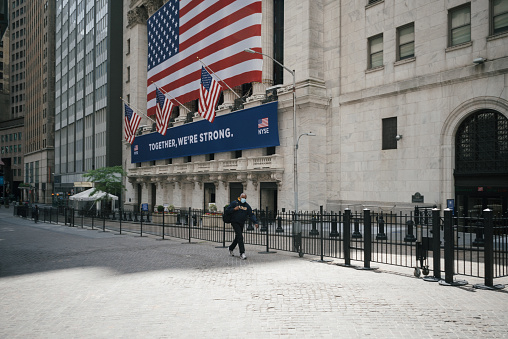 Manhattan, New York. June 01, 2020,  A man wearing a face mask walks in front of the New York Stock Exchange on an empty Broad Street in the financial district of lower Manhattan. The New York Stock Exchange reopened its trading floor to some brokers on May 26, following two months of closure due to the coronavirus pandemic.