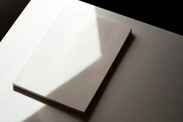 White blank magazine cover mockup, template at the corner of the table with natural light and shadow