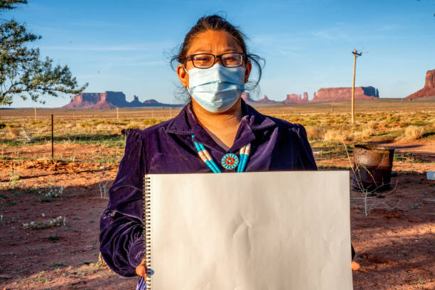 Young Navajo Girl in Monument Valley posing with a mask in front of the rock landmarks in the area wearing a Covid-19 Corona Virus Mask Holding a Blank Sign Young Navajo Girl in Monument Valley posing with a mask in front of the rock landmarks in the area wearing a Covid-19 Corona Virus Mask hopi culture photos stock pictures, royalty-free photos & images