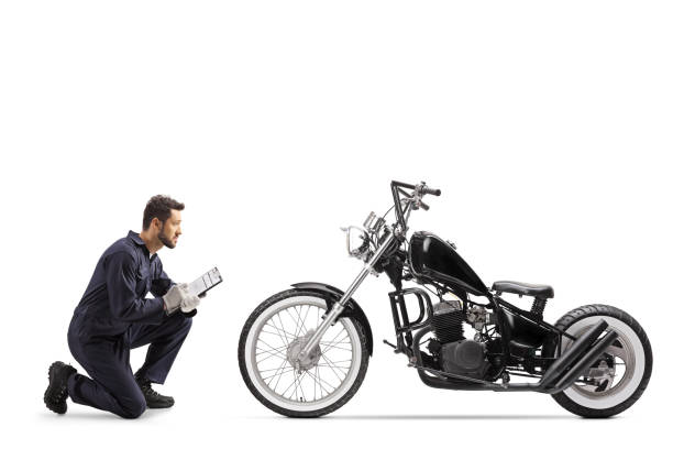 istock Motorbike mechanic in a uniform kneeling and looking at a chopper and writing a document 1247349775