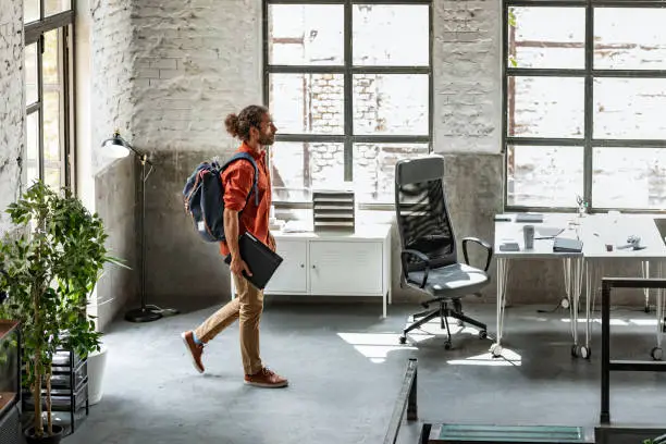 Young casual businessman holding backpack and walking into office.