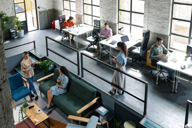 Wide Angle View of a Modern Loft Open Space Office With Businesspeople Working in It Group of young entrepreneurs/ freelancers working at a spacious open space office. coworking stock pictures, royalty-free photos & images