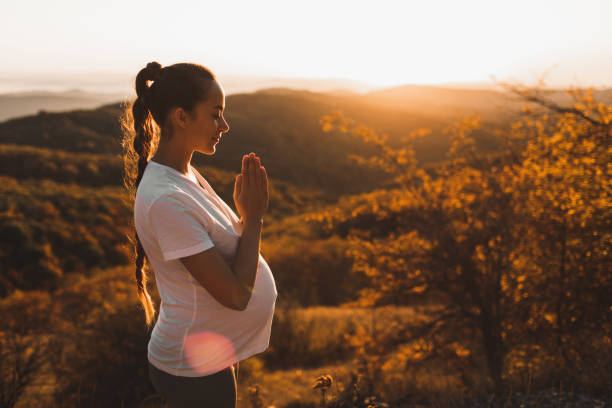 concepto espiritual y emocional de armonía con la naturaleza en el tiempo de maternidad. mujer embarazada practicando yoga al aire libre en la colina al atardecer. increíble vista a la montaña de otoño. - morning prayer fotografías e imágenes de stock