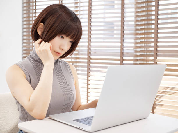 明るいリビングルームで心配しながらコンピュータを操作する日本人女性 - ブログ ストックフォトと画像