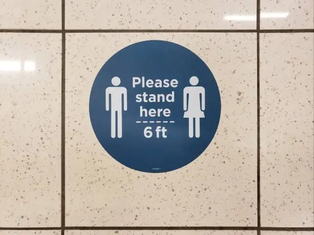 Please stand six feet apart and social distance signs in blue and white are displayed on a tile floor due to COVID-19 as businesses and retail establishments begin to reopen.