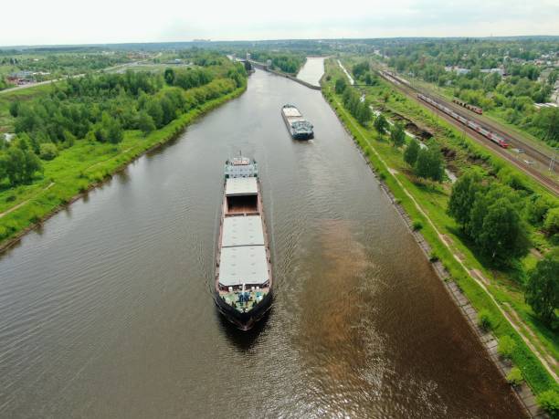 istock Beautiful panoramic landscape from high altitude two cargo commercial ships sail down the river on counter courses surrounded by green forest in summer with a sunny day 1247528355