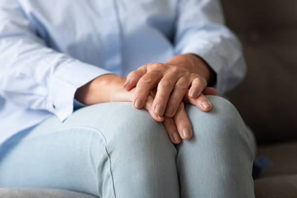 istock Old woman sitting on couch folded hands on knees closeup 1247568829