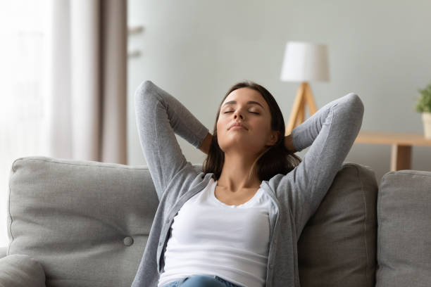 istock Calm woman puts hands behind head relaxing seated on couch 1247568841