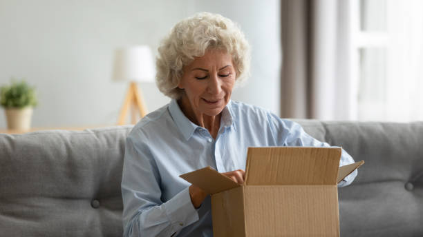 Happy senior 65s woman opens delivered parcel
