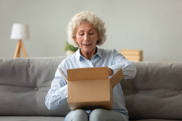 istock Elderly woman sitting on couch unpacking parcel feels satisfied 1247568844