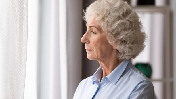 istock Old woman looking in window thinking lost in sad thoughts 1247568872