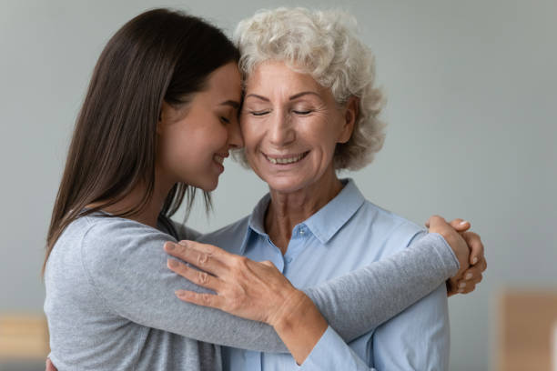 Tender moment of grownup granddaughter elderly grandmother cuddling indoors Tender moment grown up beautiful granddaughter and elderly grandmother cuddling with closed eyes enjoy time together missed each other, strong connection of multi-generational relatives women concept candid bonding connection togetherness stock pictures, royalty-free photos & images