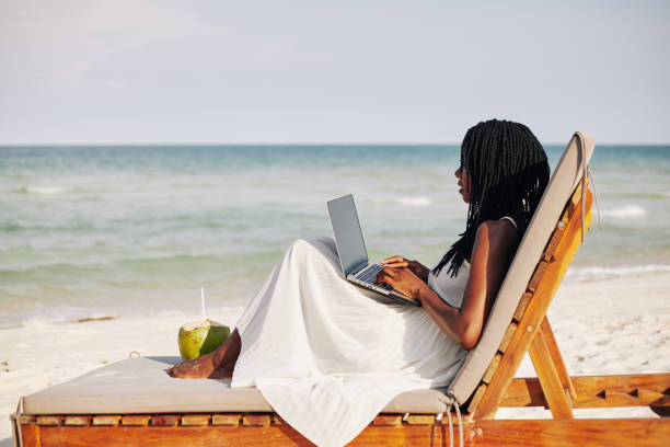 Female freelancer on beach Young woman enjoying sitting on chaise-lounge, working on laptop and looking on sea waves digital nomad stock pictures, royalty-free photos & images