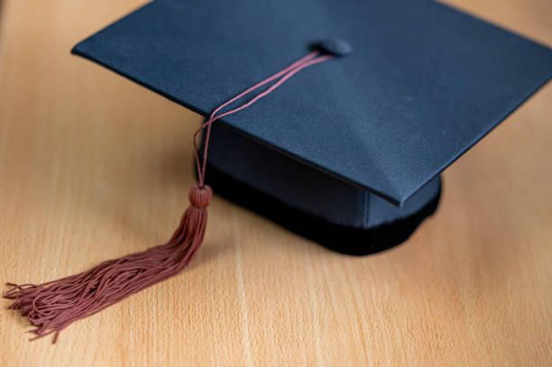 istock closeup, black graduated hat, and brown tassel placed on a wooden table 1247634785