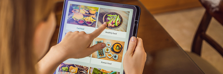 Young woman orders food for lunch online using Tablet. BANNER, LONG FORMAT