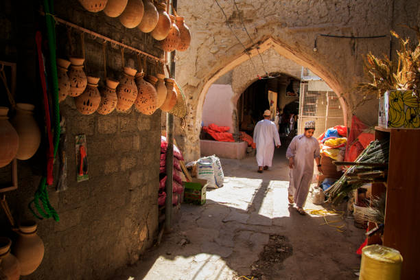 An omani boy walks past some traditional pots hangin on the wall The historic Nizwa Souq and the goat market area very cultural and vibrant souk stock pictures, royalty-free photos & images