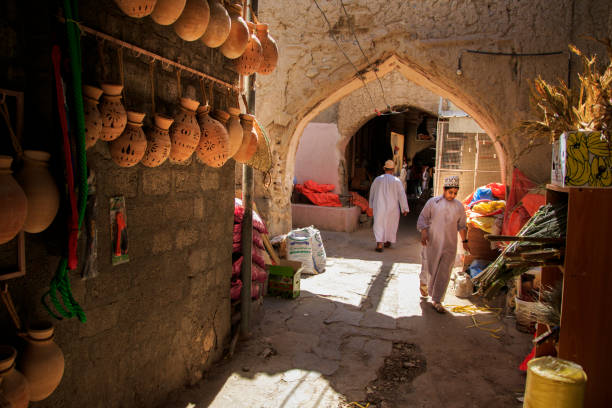 an omani boy walks past some traditional pots hangin on the wall - nizwa imagens e fotografias de stock