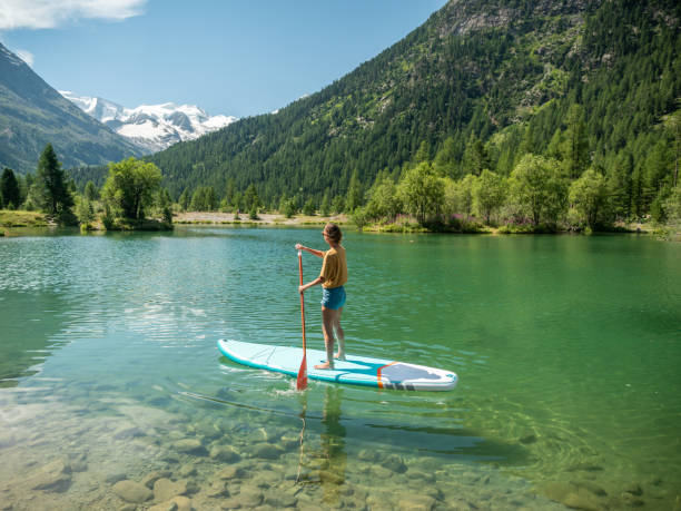 Stand up paddle with a view, woman on SUP in the mountains looking at glacier Stand up paddle with a view, woman on SUP in the mountains looking at glacier forest and mountain range. Girl enjoying outdoor activities on alpine lake paddleboard photos stock pictures, royalty-free photos & images