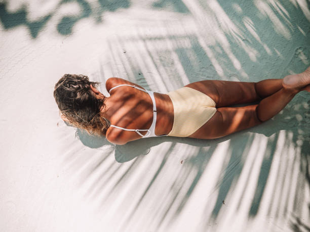 Young woman lying down on white sand beach, palm tree shadows on her back Young woman lying down on white sand beach, palm tree shadows on her back making sun light contrast. Skin care sun tan summer UVA protection on tropical vacation tan skin stock pictures, royalty-free photos & images