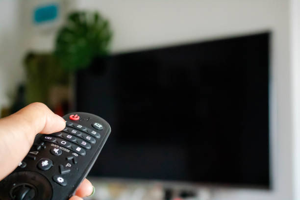 istock Watching Television Concept. Hand using a remote control in front of the TV screen. Relaxation in Modern Living Room. Focus on Remote. copy space. 1247660170