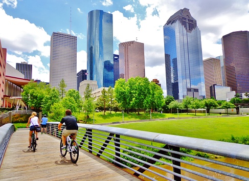 Young Man and Woman Riding Bikes on Small Wooden Bridge in Houston's Buffalo Bayou Park (view of river and skyline of downtown Houston) - Houston, Texas, USA
