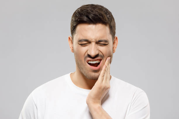 istock Young guy with closed eyes suffering from severe toothache, touching jaw with fingers trying to ease strong tooth pain, isolated on gray background 1247693966