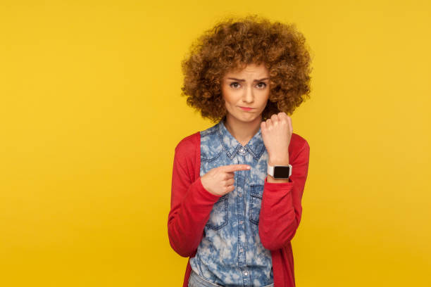 портрет расстроен нетерпеливой женщины с вьющимися волосами, показывающими наручные часы и выглядями разочарованными в к�амере - checking the time women impatient wristwatch стоковые фото и изображения
