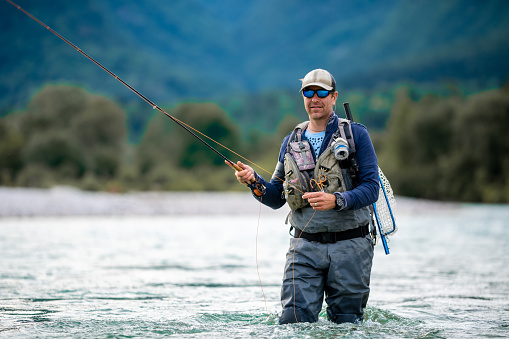 Close up of a fly fisherman casts his line while wading in the middle of a river