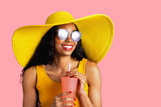 retrato de una joven mujer sonriente con sombrero amarillo de verano y gafas de sol sosteniendo una taza de bebida y paja de papel - pink hat fotografías e imágenes de stock