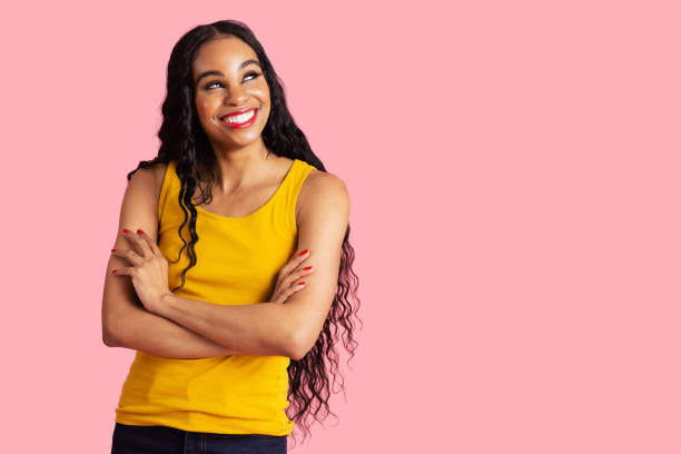 Portrait of a confident young woman with long black curly hair smiling with arms crossed and looking up Portrait of a confident young woman with long black curly hair smiling with arms crossed and looking up black woman hair extensions stock pictures, royalty-free photos & images