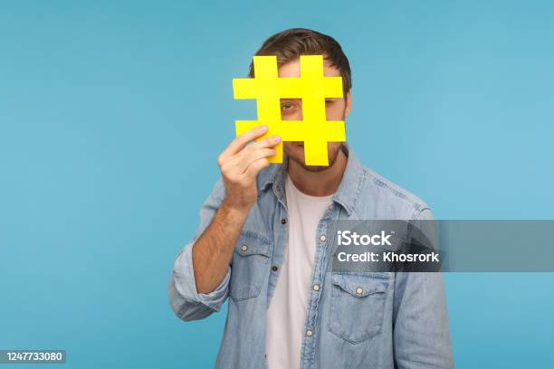 Porträt Des Mannes Im Jeanshemd Der Durch Das Große Gelbe Hashtagsymbol Schaut Isoliert Auf Blauem Hintergrund Stockfoto und mehr Bilder von Hashtag