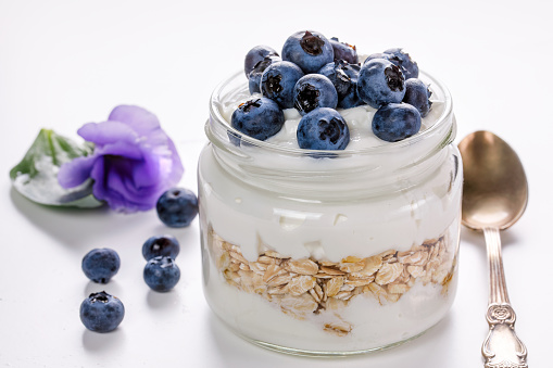 Healthy breakfast - yogurt with blueberries and muesli served in glass jar, on color white background