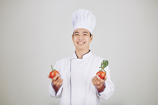 Portrait of happy handsome young chef in uniform holding fresh ripe tomatoes