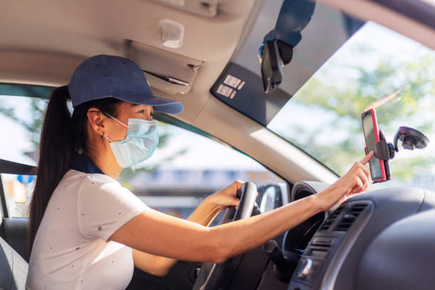 Hardworking Woman Driving Car for Rideshare Asian female Car sharing driver checking on the mobilephone searching for job destination, woman wearing face mask while driving crowdsourced taxi photos stock pictures, royalty-free photos & images