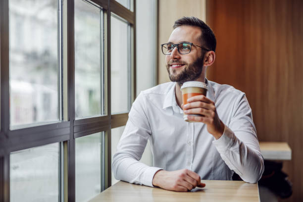 istock Young handsome bearded elegant man sitting in cafeteria and drinking fresh morning coffee from disposable cup. 1247754646