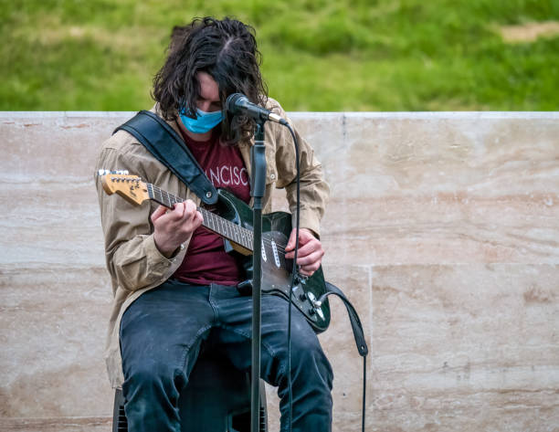 junger mann mit langen haaren spielt gitarre. straßenkünstler auftreten. - men artist guitarist guitar stock-fotos und bilder