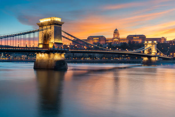 il castello di buda con il ponte a catena szechenyi in primo piano riflette nel danubio durante il tramonto - budapest chain bridge night hungary foto e immagini stock