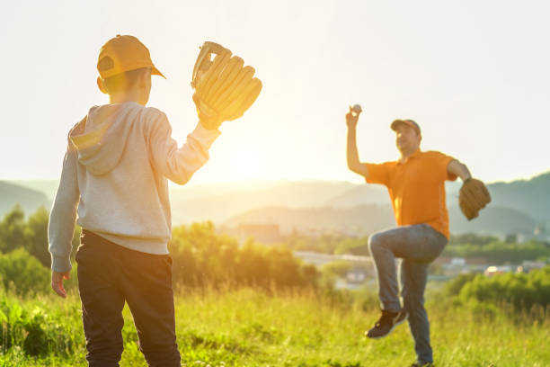 father and son playing in baseball. playful man teaching boy baseballs exercise outdoors in sunny day at public park. family sports weekend. father's day. - baseballs baseball baseball catcher catching imagens e fotografias de stock