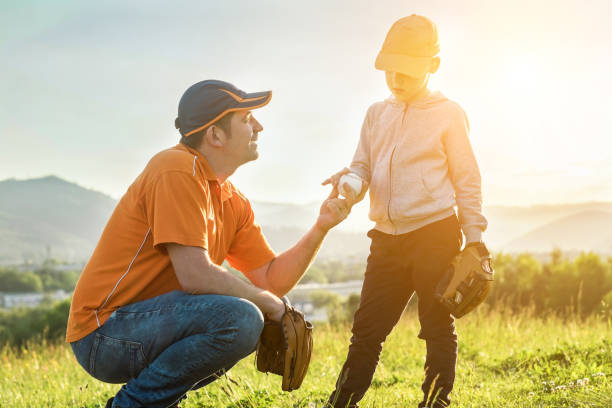 vater und sohn spielen im baseball. verspielter mann, der boy baseballs beibringt, übt sich im freien an sonnigen tagen im öffentlichen park. familiensportwochenende. vatertag. - baseballs catching baseball catcher adult stock-fotos und bilder