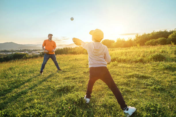 istock Father and son playing in baseball. Playful Man teaching Boy baseballs exercise outdoors in sunny day at public park. Family sports weekend. Father's day. 1247783302