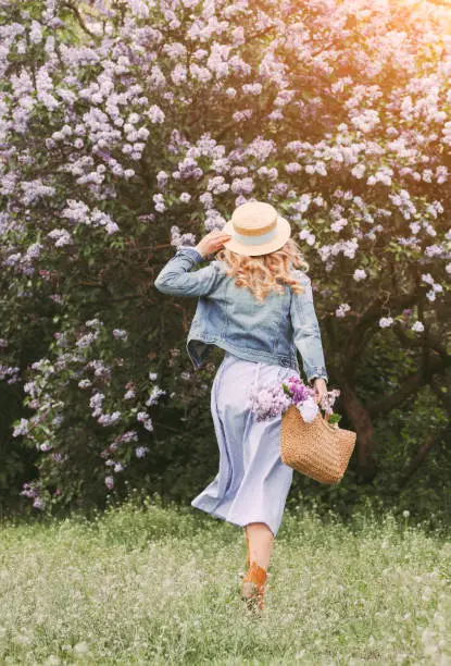 Photo of Young carefree hipster girl in stylish dress have fun on blossom lilac garden