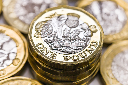 London, England - April 2019: Close up view of a one pound coin in the British currency. One coin is surrounded by other coins. The abbreviation for the currency is 