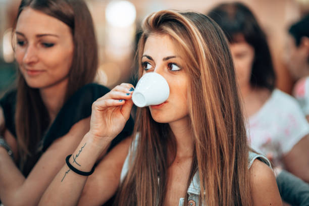 Happy beautiful ladies sitting together outdoors in cafe and enjoying drinking tea from pink cups closeup. Holiday party, celebration, event, friendship, best friends, attractive women.