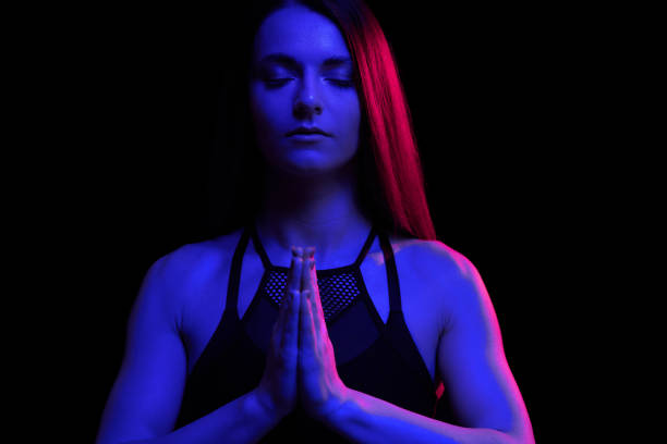 Young fit woman meditating. Neon light. Modern sci fi representation of yoga. Copy space. stock photo