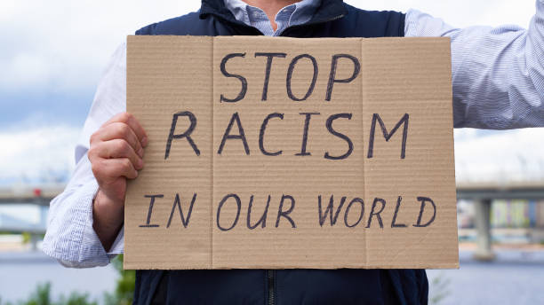 istock Stop racism concept. Unrecognizable white person holds sign with text against racist. 1247847490