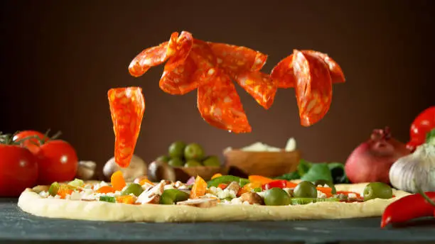 Falling raw ingredients on pizza, freeze motion. Italian traditional meal.