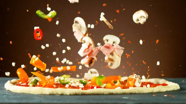 Falling raw ingredients on pizza, freeze motion. Italian traditional meal.